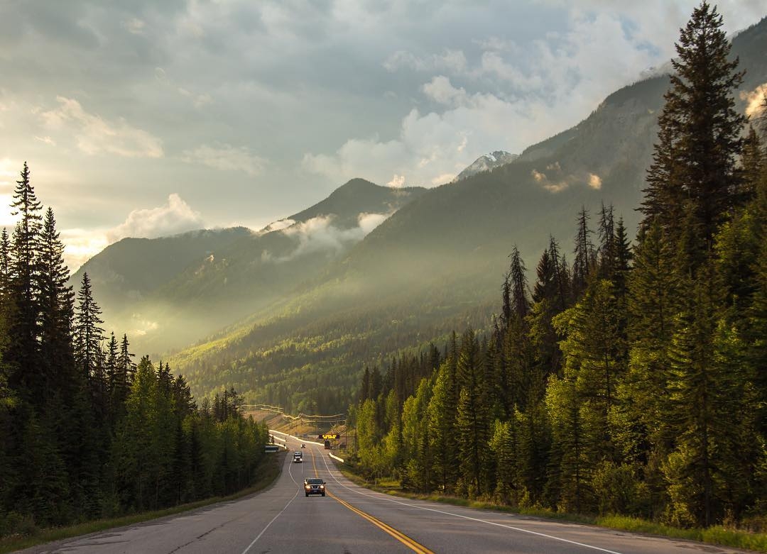 A highway stretches past a stunning mountainous landscape at sunset.